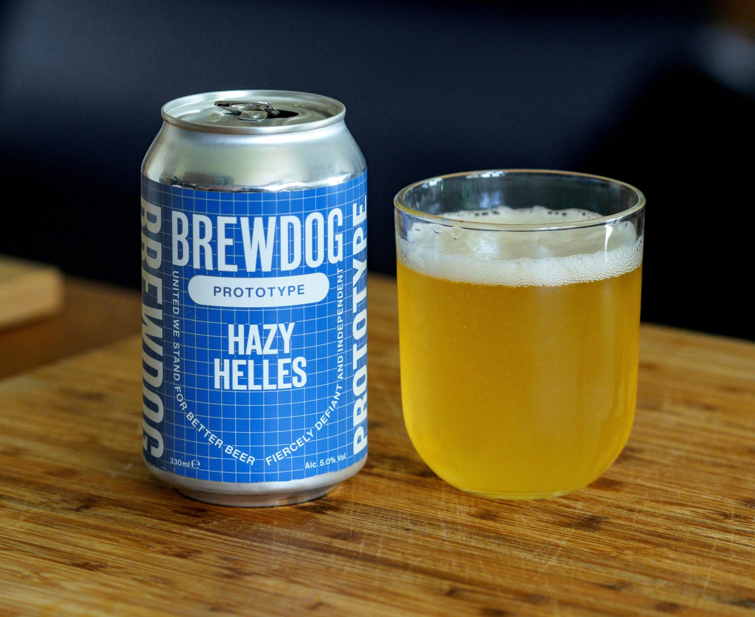 Close-up of BrewDog Hazy Helles prototype beer in a can and glass on a wooden surface.