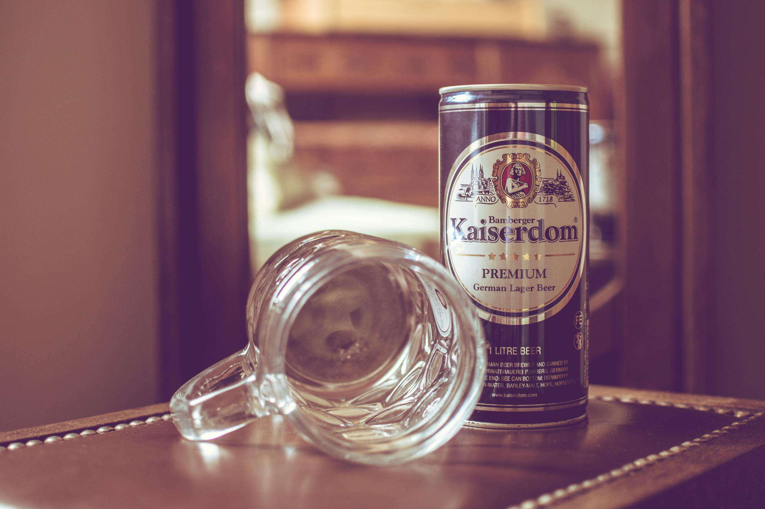 A vintage-style photo of a Kaiserdom beer can and glass mug on a polished table.